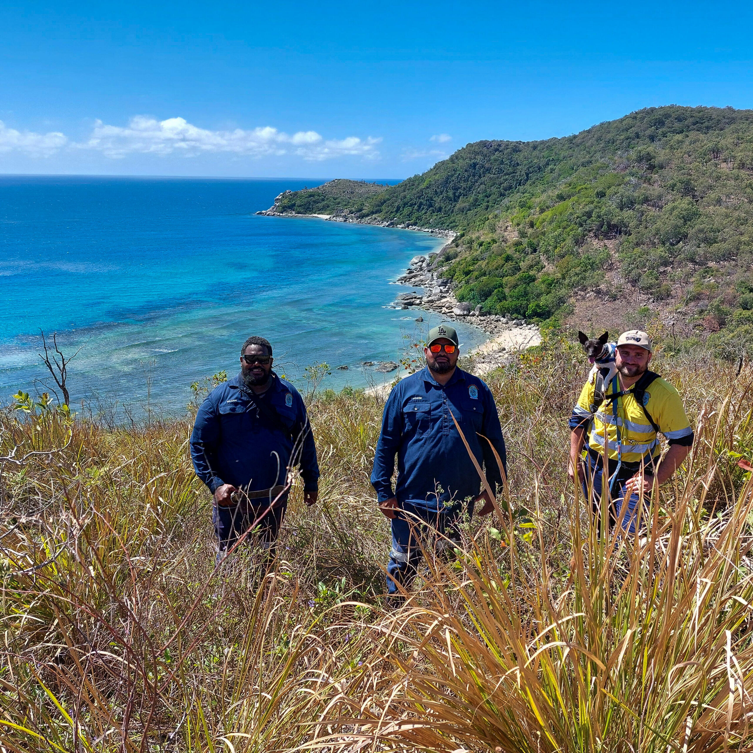 Three Indigenous rangers pictured in front of a beautiful beach is Palm Island. 