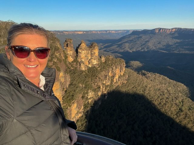 Selfie of senior consultant Dr Alli Anderson in front of the warmly light three sisters, Blue Mountains. 